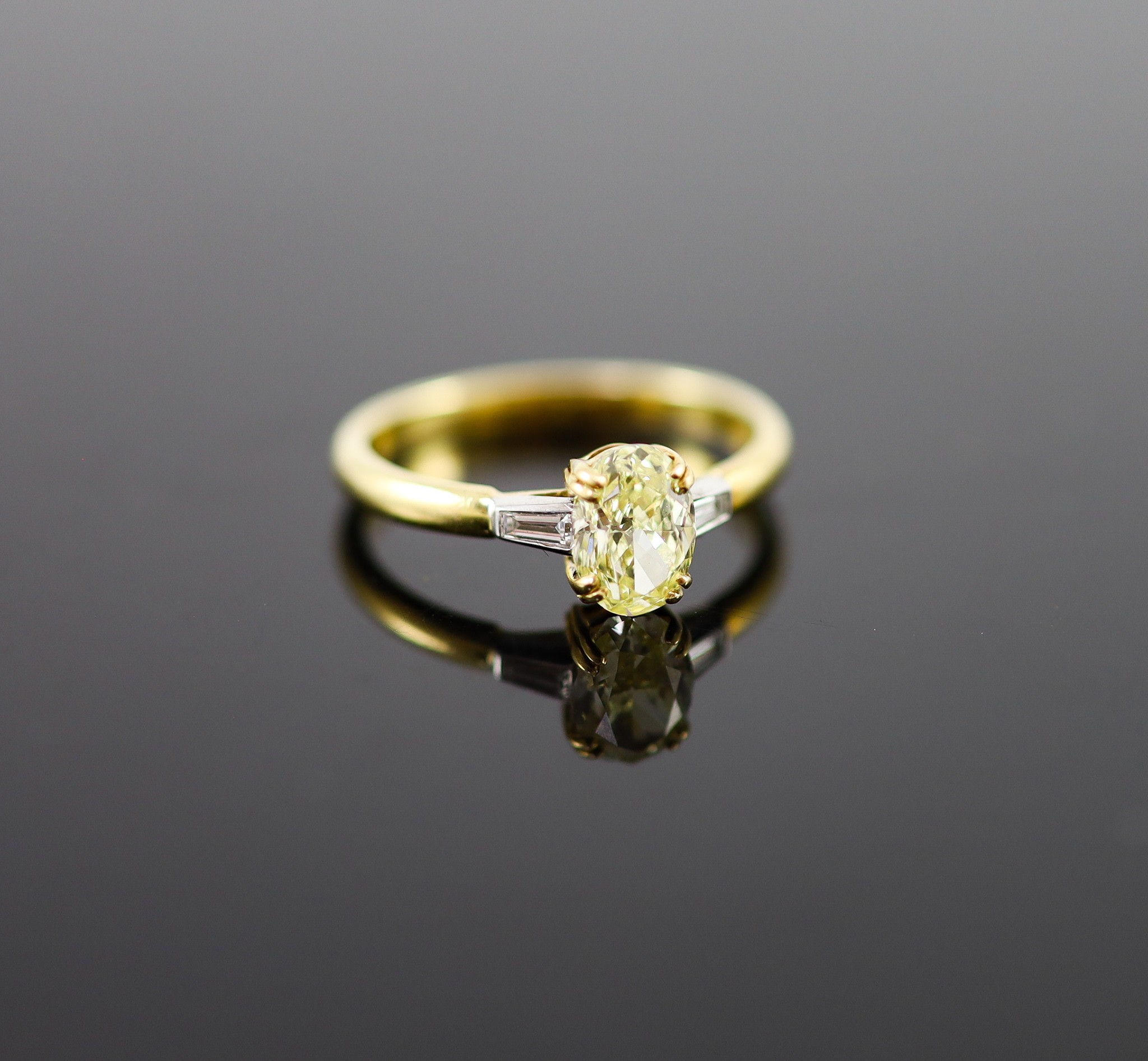 A modern 18ct gold and single stone oval fancy yellow diamond ring, with trapeze cut diamond set shoulders